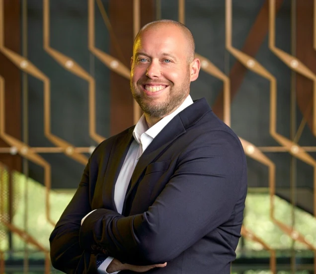 Corporate portrait of cheerful executive standing in front of decorative wooden wall pattern