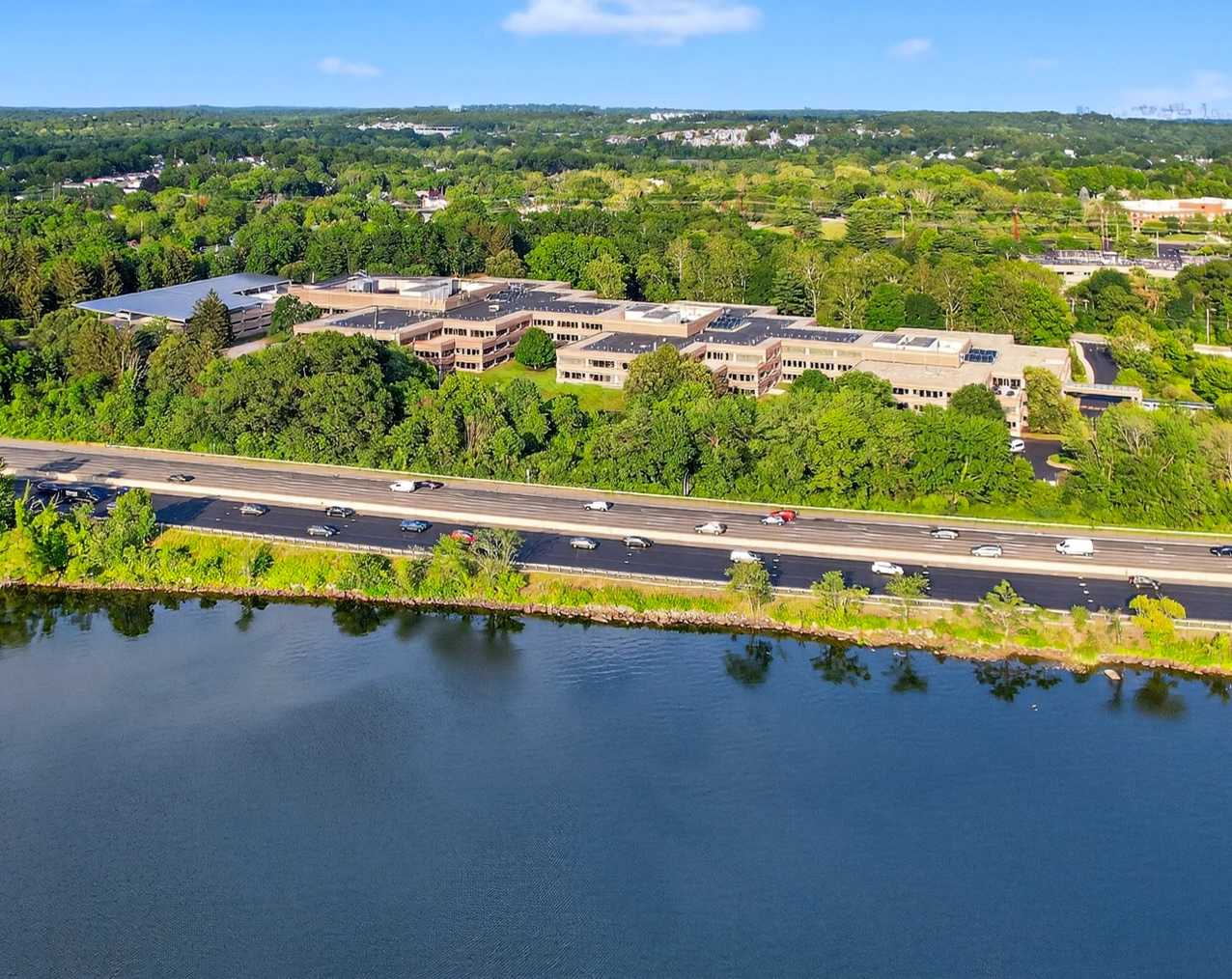 Aerial view of office campus surrounded by trees, located beside highway and scenic waterfront